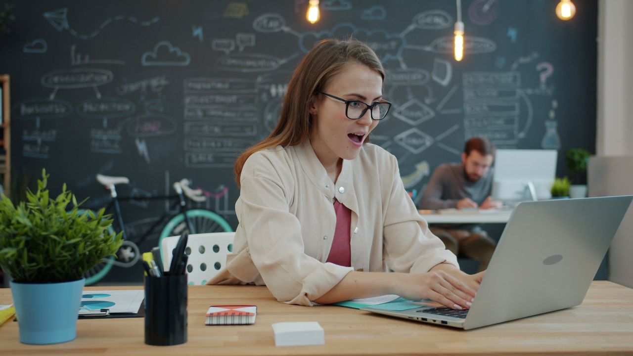 services-01 Smiling woman in office amazed by laptop, creative workspace with blackboard in background.
